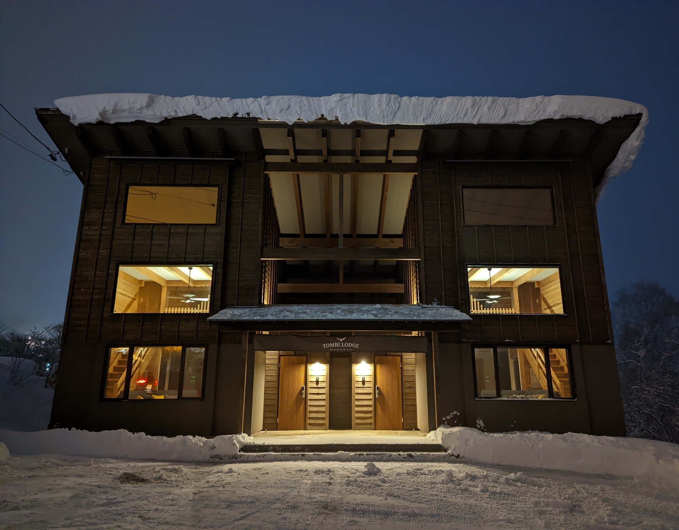 大雪のあとの夕暮れどきのトンビロッジ。すべての窓に明かりが灯り、看板の下で2つの玄関が光っている