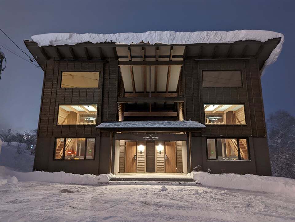 Tombi Lodge on a snowy winter night, with lights on inside and snow on the roof
