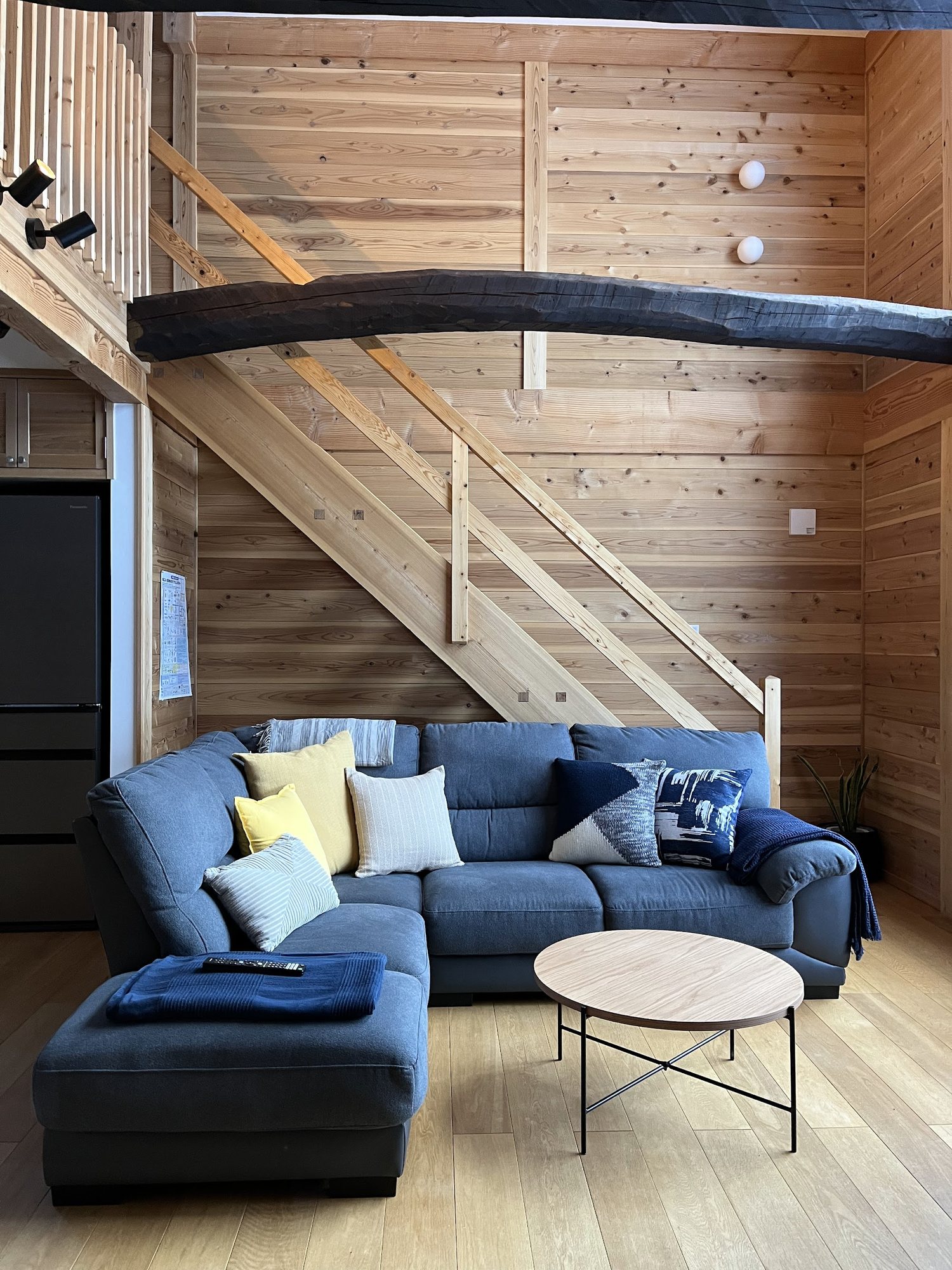 Double-height living space with the sofa, timber stairs and an old dark beam overhead