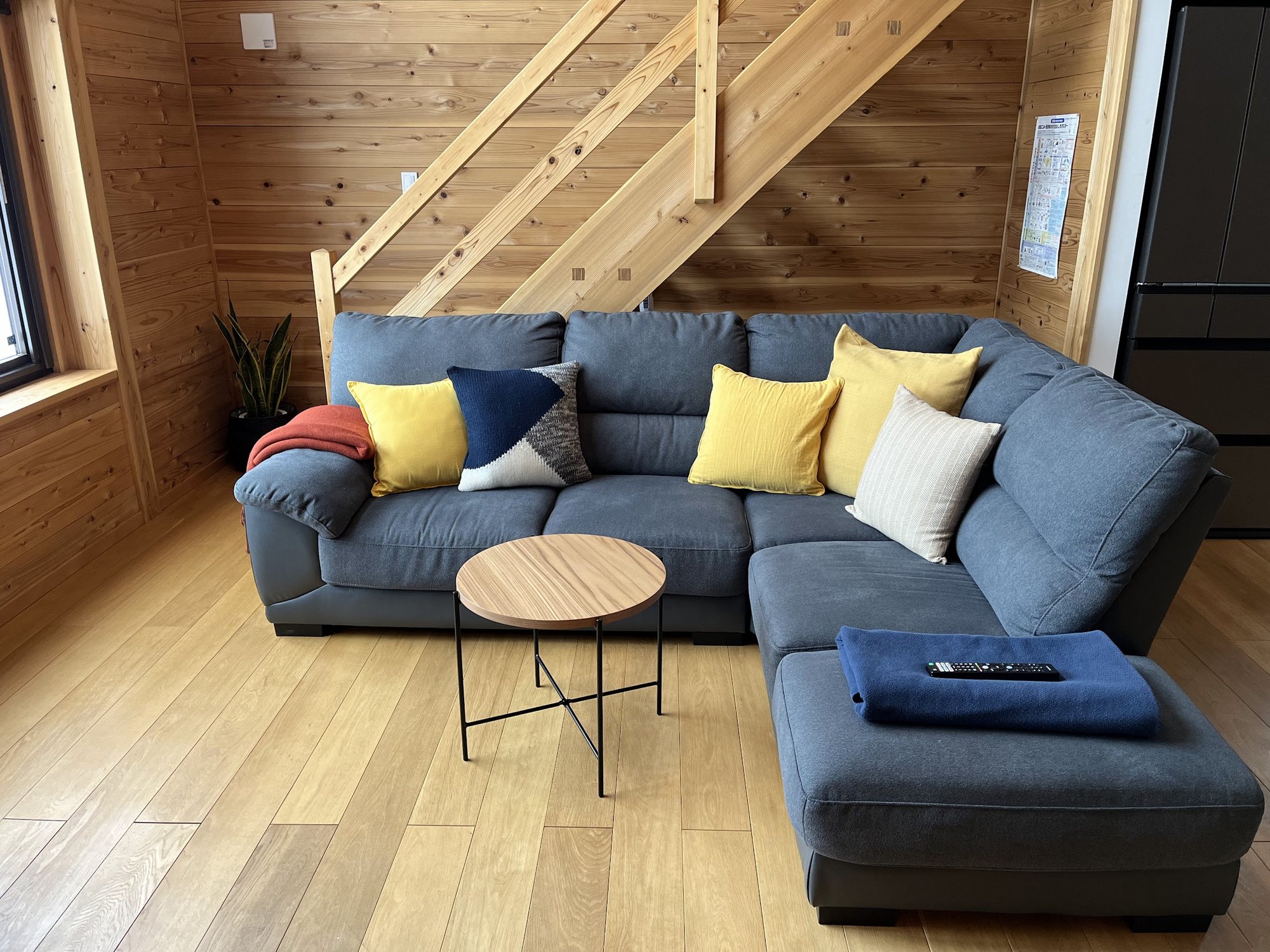 Blue corner sofa with yellow cushions and a round coffee table below the timber stairs
