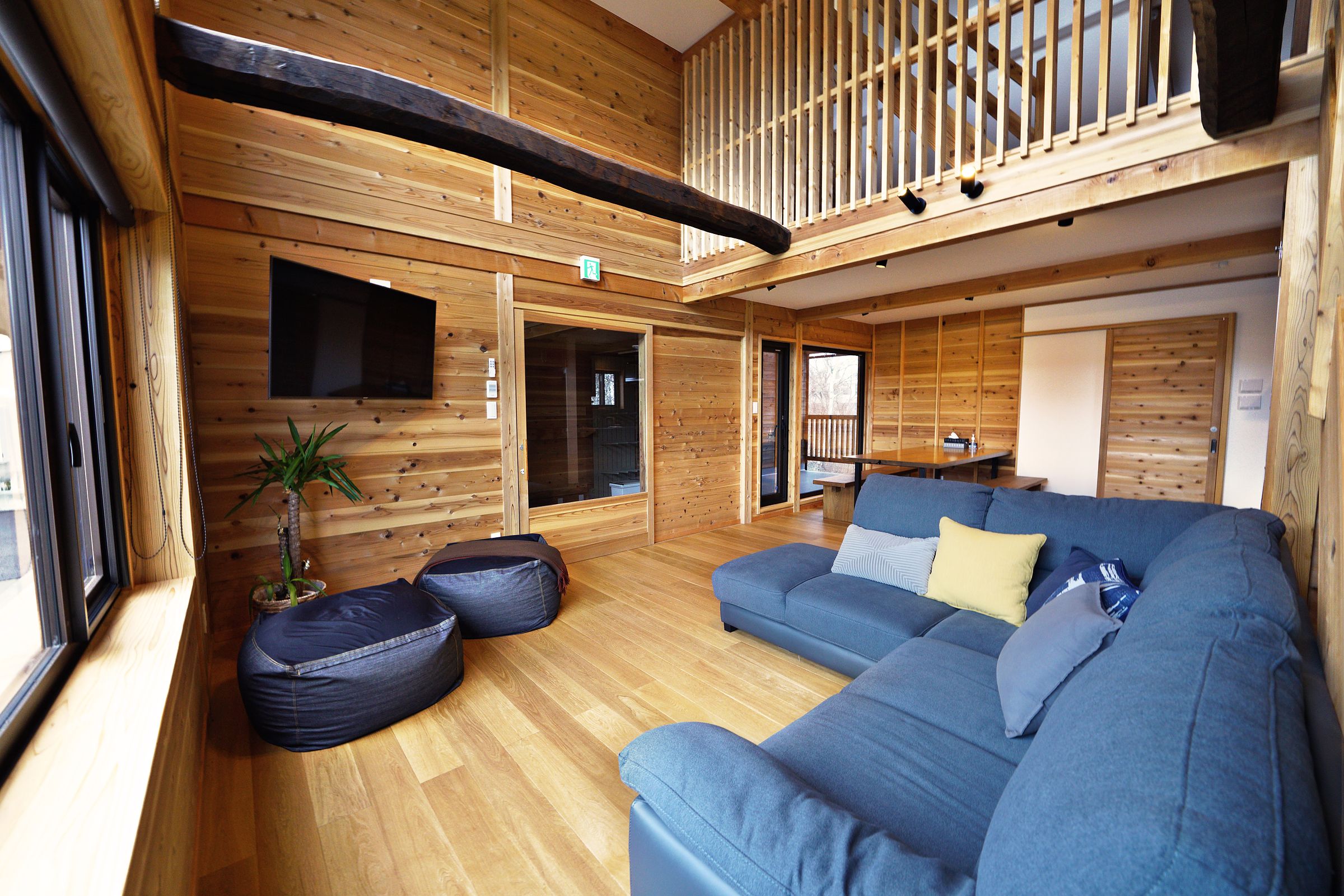 Living room with a blue corner sofa, beanbags and timber walls under the loft